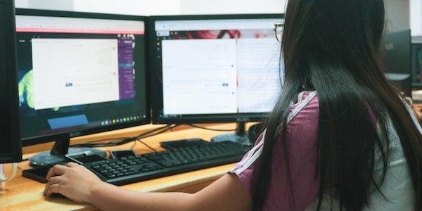 woman sitting at desk with two monitors